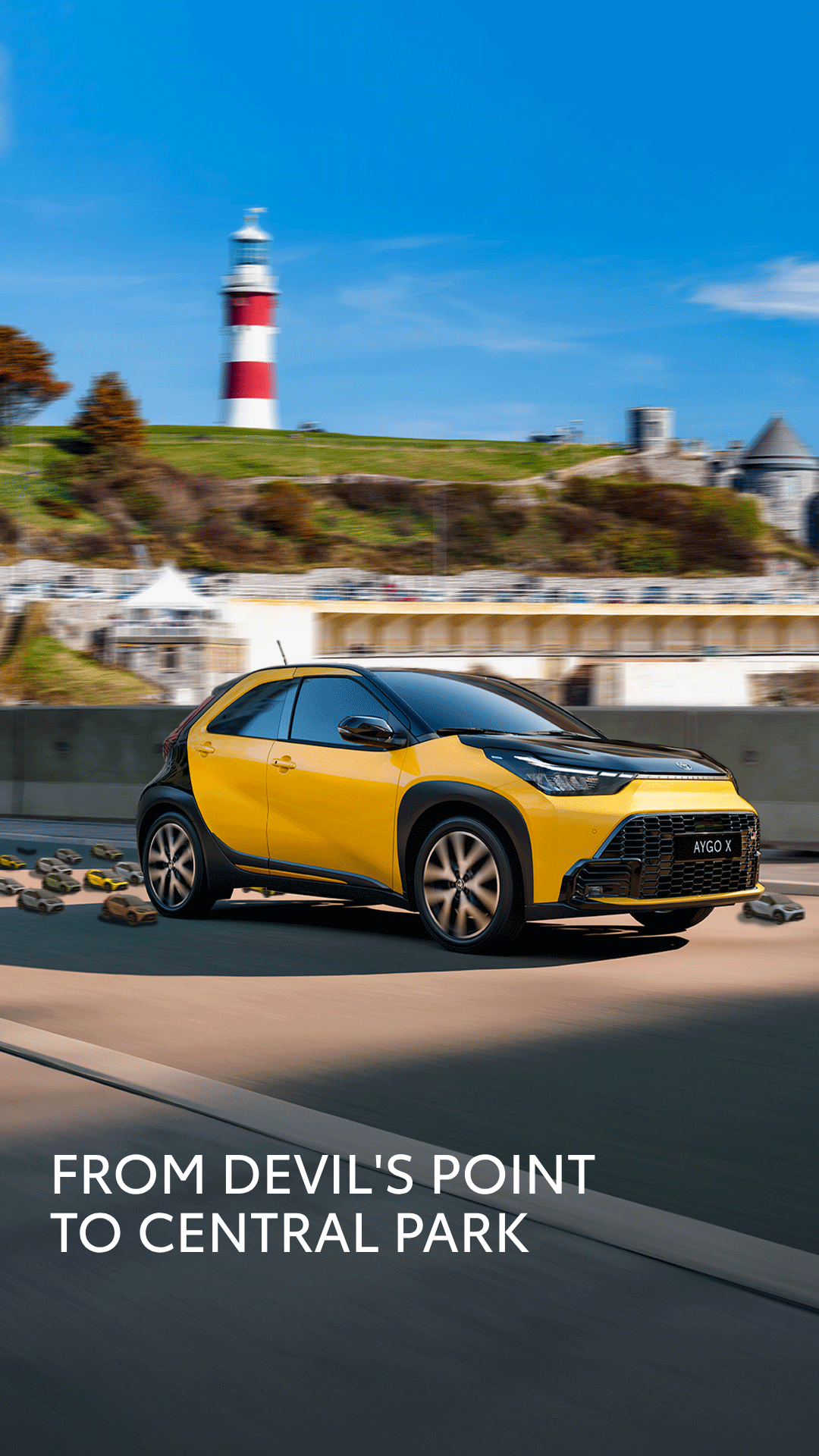 Yellow compact car racing along a highway with a coastal lighthouse and cliffs in the background; ad text reads 'From Devil's Point to Central Park' at the bottom.